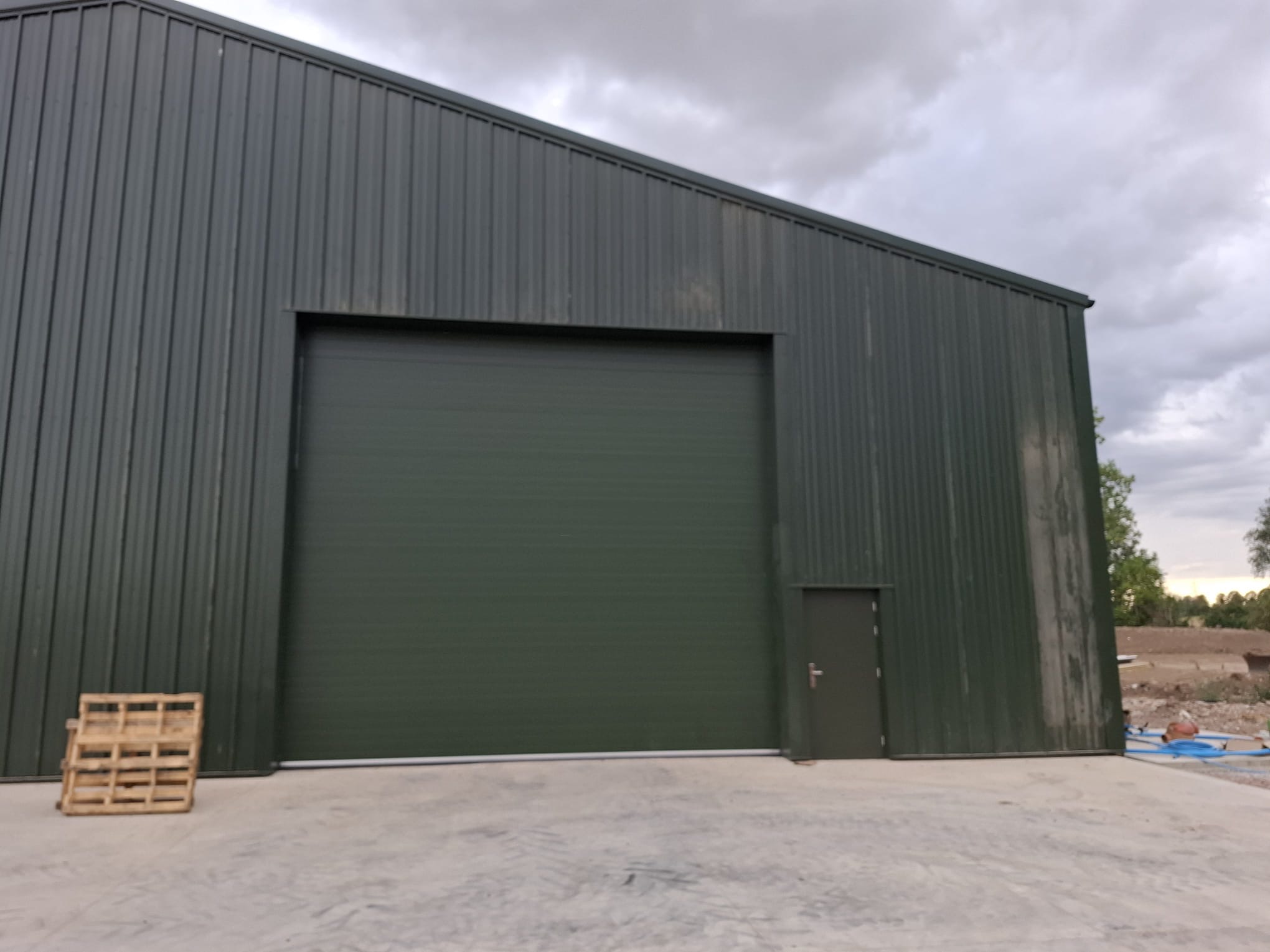 Dark green profiled metal clad industrial building with roller shutter door - DB Roofing project