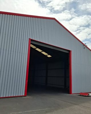 Industrial steel-framed building with grey profiled metal cladding and red trim - DB Roofing project